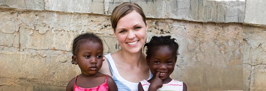 A female on a missions and ministry trip with two young children on her lap.