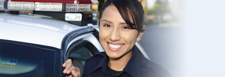 A female police officer with a criminal justice degree standing in front of police car.