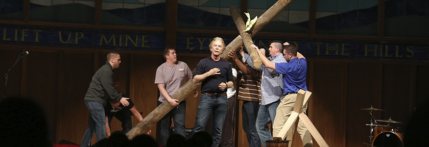 Bachelor in Christian studies degree students holding a wooden cross on stage during a sermon.