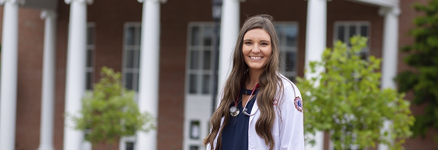 A female bachelor's in public health degree student standing on the University of the Cumberlands campus smiling.