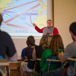 Dr. Coleman pointing to a projector with students facing him in the foreground.