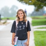 Young woman wearing backpack standing outdoors.