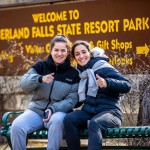 Two young women sitting next to each other, giving thumbs-up signs.