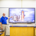 professor in front of screen with rocketship