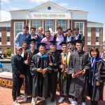 Students wearing cap and gown with friends behind