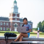 A student finishes homework while sitting outside on campus. 