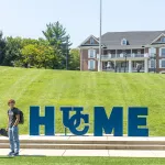 A student stands with a skateboard near Cumberlands HOME sign.