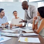 A group of business professionals discuss a project around a table.
