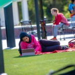 A female student relaxes on campus while using a computer. 