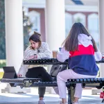 Two girls studying outside on a bench. 