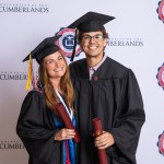 A female and male student pose with their diplomas after graduating. 