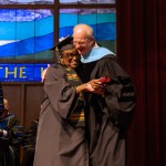 A female graduate hugs the university president after receiving her degree. 