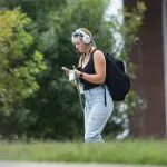 A female student with a backpack looks at her phone after leaving class.