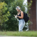 A female student with a backpack looks at her phone after leaving class.