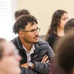 A male student with glasses listens to a speaker during the annual business forum. 