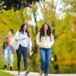 Two female students talk as they walk across campus on a fall morning. 