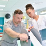 A female occupational therapist assists a man on a strength machine. 