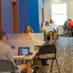 Several students sit at study desks inside the campus library with book shelves to their right. 