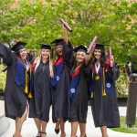 A group of five females in regalia celebrate with their diplomas following commencement services. 