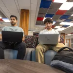 Two male executive students use their computers while in the student success center. 