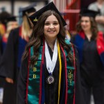 A female student walks with other graduates into the spring graduation ceremony. 
