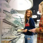 Two female students chat while standing in line in the cafeteria. 