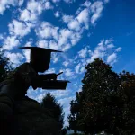 A statue on campus is shaded in the foreground with a dramatic blue sky behind it. 