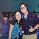 A couple pose for the camera wearing headphones during a dance on campus.