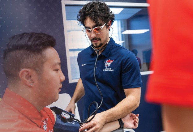 Two male DPT students check blood pressure during a clinical lab. 