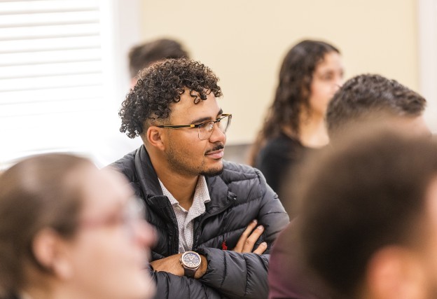 A male student with glasses listens to a speaker during the annual business forum. 