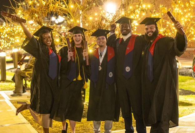 Five students pose in their caps and gowns while holding their diplomas following Cumberlands December graduation ceremony. 
