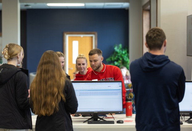 A group of students watch a male student demonstrate using AI during an info session in the student center. 