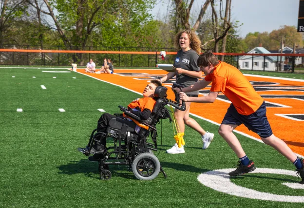 A male high school student, being coached by a Cumberlands student volunteer, pushes a child in a wheel chair during the 2026 Special Olympics.